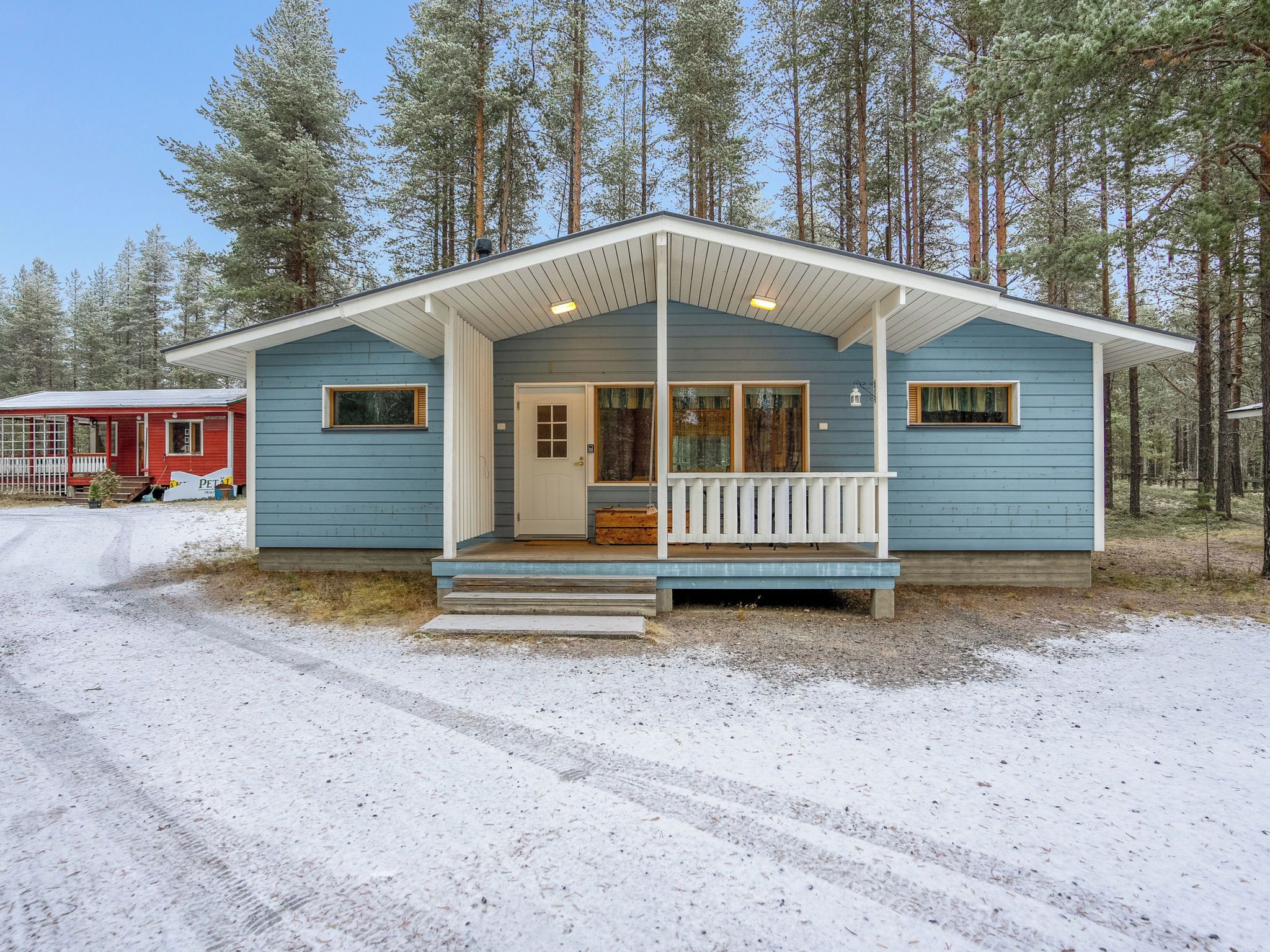 A two-story cabin with a porch, surrounded by a forest.