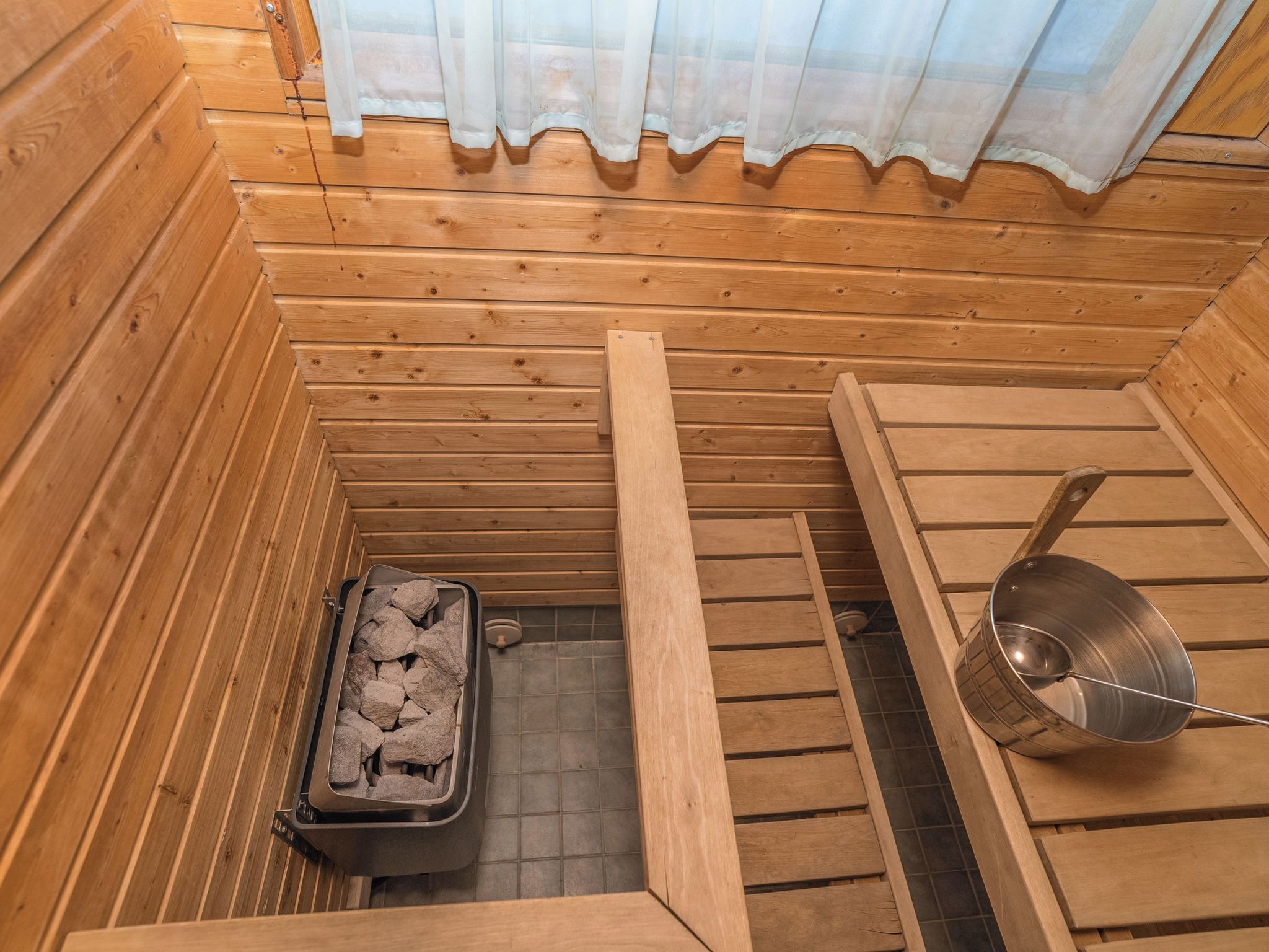 Une salle de sauna avec des murs en bois, un banc, un récipient en métal rempli de pierres et un bassin en métal.