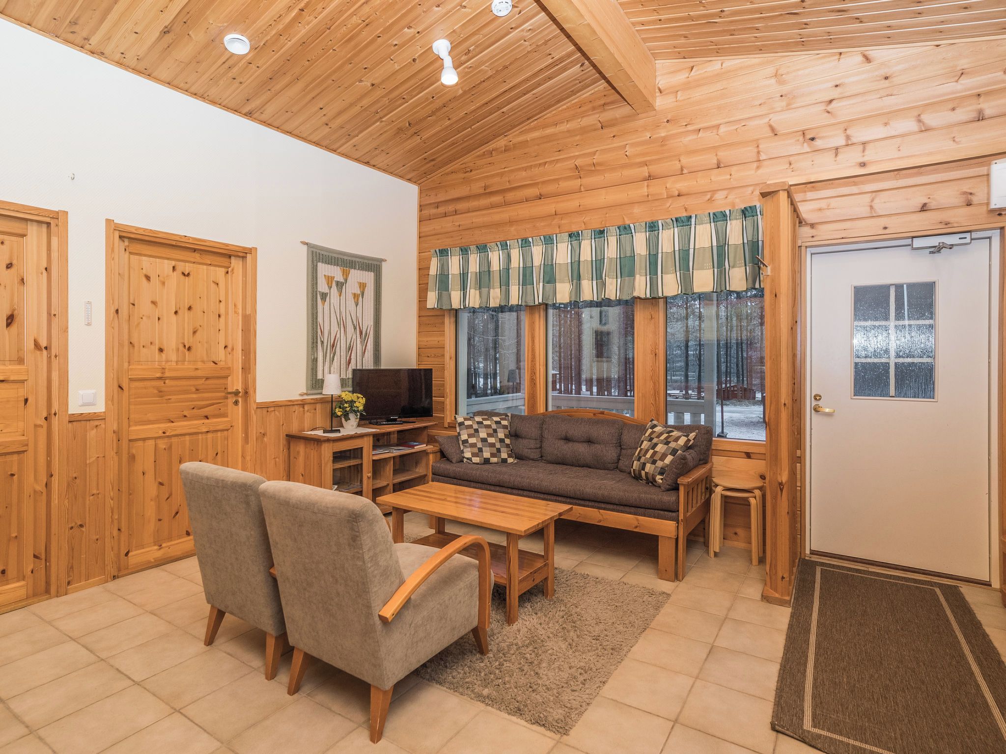 A wooden interior with a sofa, chairs, a TV, and a window with a view of trees.