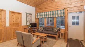 A wooden interior with a sofa, chairs, a TV, and a window with a view of trees.