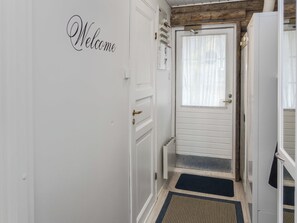 Un couloir avec une pancarte « Bienvenue », une porte avec une fenêtre et un paillasson à l’entrée.