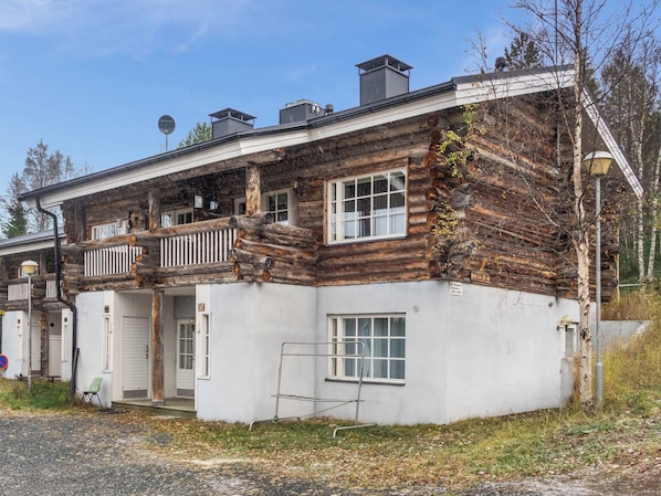 A two-story log cabin with a balcony, white exterior walls, and a metal railing.