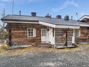 Une cabane en rondins avec un porche à l’avant, une cheminée et une antenne parabolique.