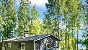 Une cabane avec un toit en pente, une cheminée et une véranda dotée d’une seule fenêtre.