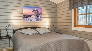 Une chambre à coucher comprenant un lit, une table de chevet, une lampe, une fenêtre donnant sur des arbres et un tableau accroché au mur.