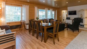Un interior de madera con una mesa de comedor rodeada de sillas, un sofá y un televisor montado en la pared.