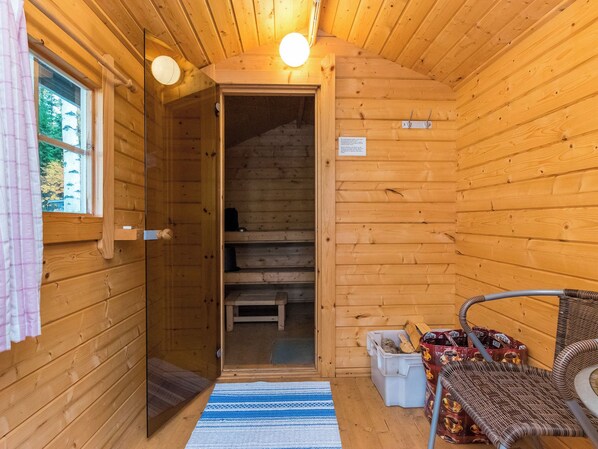 A wooden cabin interior with a visible door leading to a staircase, a bench, and a small table with items on it.