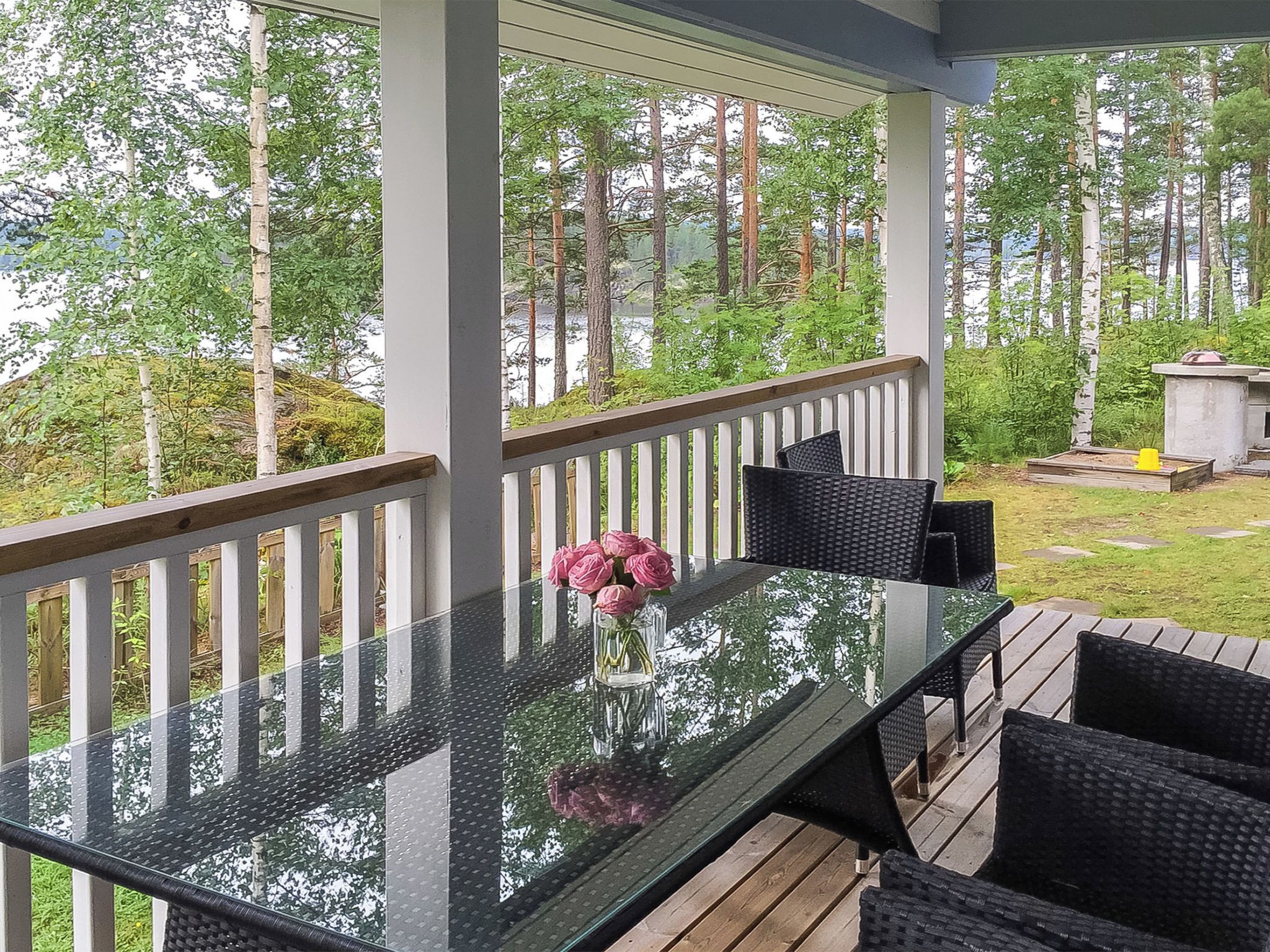 A covered outdoor deck with a glass-top table, surrounded by chairs, and a small flower vase.