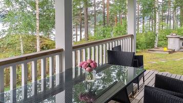 Een overdekt terras met een tafel met glazen blad, omringd door stoelen en een kleine bloevas.