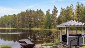 A gazebo with a roof and steps leading up to it, situated by a calm lake with a dock and a small boat. - Kiikkukallio by Interhome (Rautalampi)