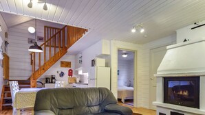 A cozy living room with a leather sofa, a fireplace, wooden flooring, and a staircase leading to an upper level. - Kiikkukallio by Interhome (Rautalampi)