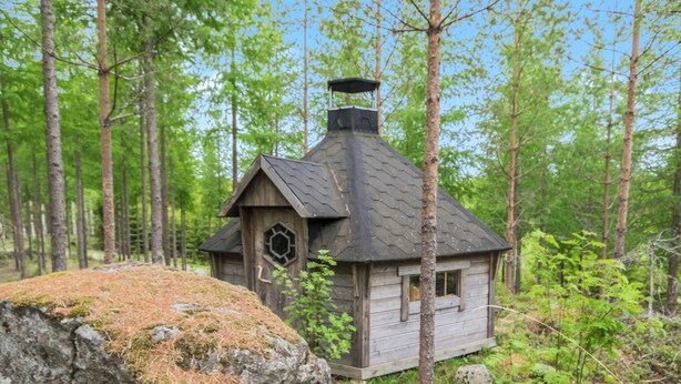 A wooden hut with a hexagonal window and a chimney, surrounded by a forest. - Kiikkukallio by Interhome (Rautalampi)