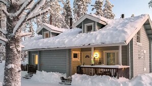 Una cabaña cubierta de nieve con un porche y escalones que conducen a la entrada.