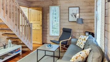 Et trægulv med trappe, sofa, stol, bord og et billede i ramme på væggen.