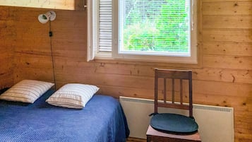 Quarto com cama, uma cadeira e janela com persianas.