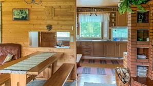 L’intérieur d’un chalet accueillant, avec une table à manger en bois, des bancs, un canapé, un coin cuisine doté de placards, une cheminée en briques et une fenêtre avec des stores.