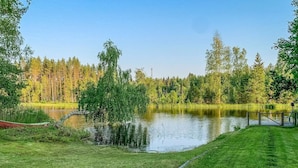 Une vue paisible sur un lac, avec une zone herbeuse, un petit bateau et une jetée en bois.