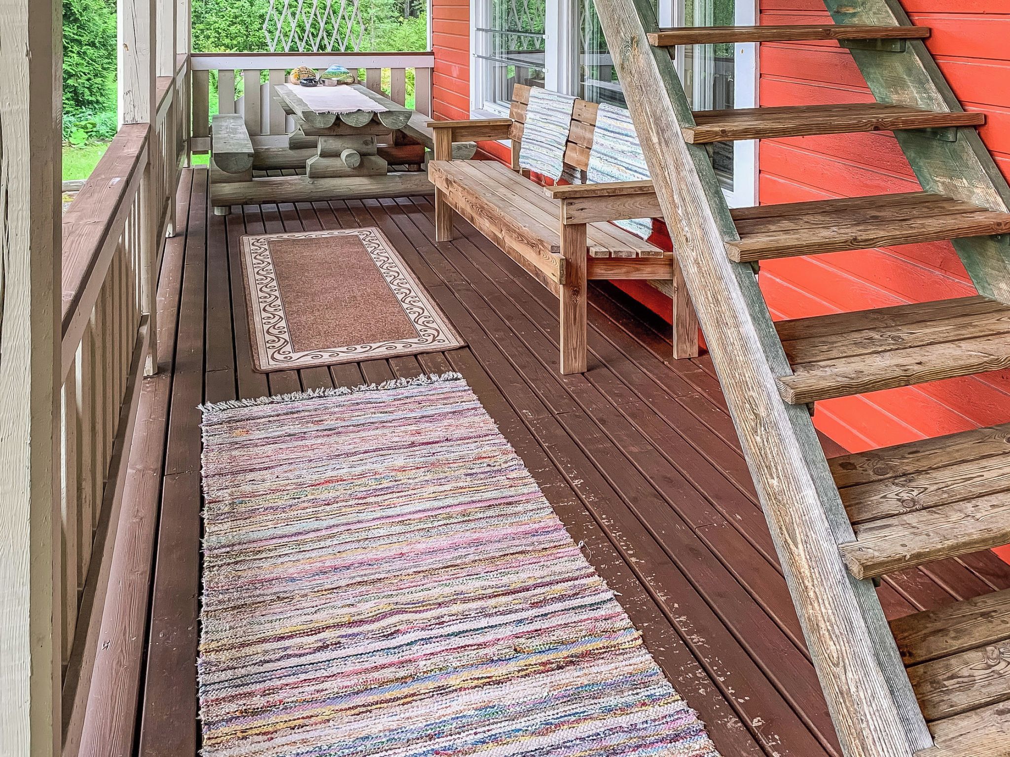 A wooden deck with a bench, a table, and a rug.
