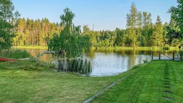 Un entorno tranquilo junto al lago, con una zona de césped, un muelle de madera y un bosque denso al fondo.