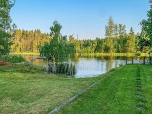 Un entorno tranquilo junto al lago, con una zona de césped, un muelle de madera y un bosque denso al fondo.
