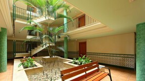 Un amplio atrio interior con una fuente central, varios niveles con balcones y un banco de madera.