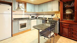 Cocina compacta con refrigerador, microondas, horno y comedor con mesa y sillas.