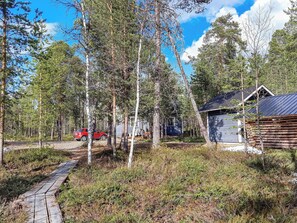 A forested area with a wooden cabin, a red car, and a paved path. - Hoviranta by Interhome (Inari)