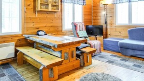 A cozy cabin interior with a wooden dining table, a blue sofa, and a television. - Hoviranta by Interhome (Inari)