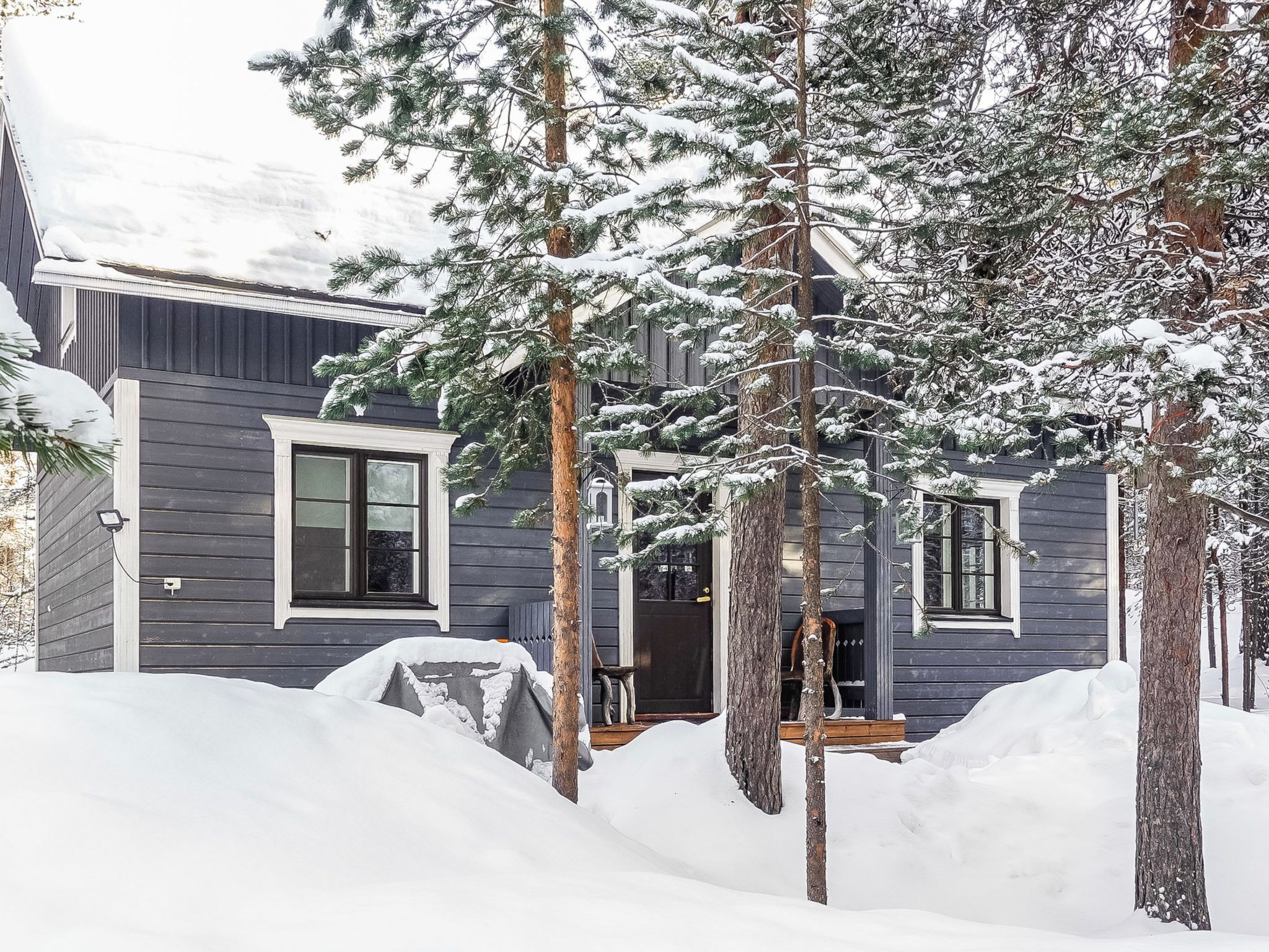 Een modern, twee verdiepingen tellend huis met een donkere buitenkant, omgeven door met sneeuw bedekte grond en bomen.