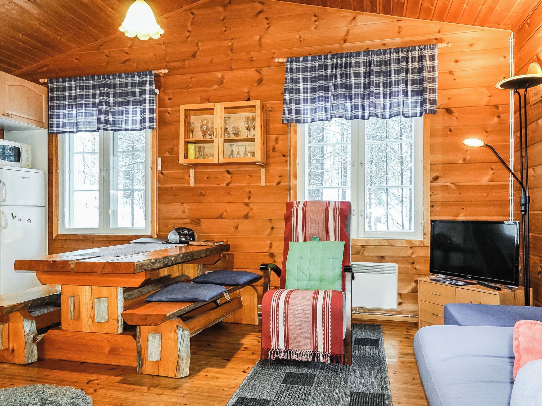 L’intérieur d’un chalet accueillant, avec une table à manger en bois, un fauteuil rembourré, un canapé et un téléviseur.