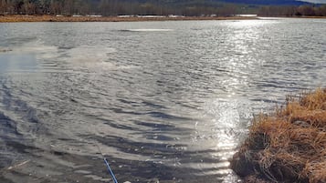 Un cuerpo de agua con una caña de pescar en la orilla, rodeado de un paisaje natural con colinas al fondo.