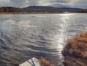A body of water with a fishing rod on the shore, surrounded by a natural landscape with hills in the background. - Hoviranta by Interhome (Inari)