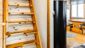 A wooden ladder leading to a lofted sleeping area, a black cylindrical object, and a wooden table in a cabin interior. - Hoviranta by Interhome (Inari)