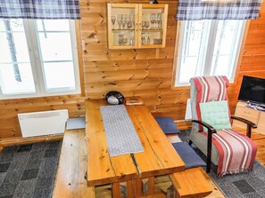 Interior acogedor de una cabaña con una mesa de comedor de madera, una silla con cojín a rayas y un aparador de puertas de cristal que exhibe varios vasos.