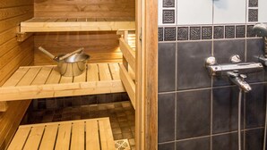 A wooden sauna with a metal bucket and a shower area with a faucet and showerhead.