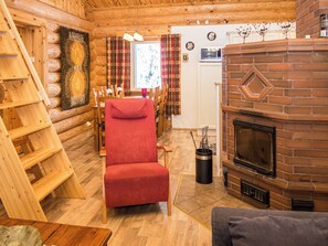 A cozy log cabin interior with a fireplace, a red chair, wooden shelves, and a dining area.