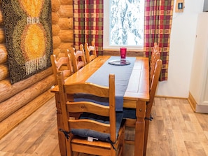 A wooden dining table with chairs, a placemat, and a red glass.