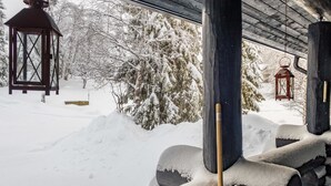 A snow-covered log cabin with a wooden porch and two lanterns.