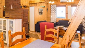 A cozy wooden cabin interior with a dining area, sofas, and a fireplace.