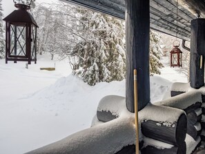 A snow-covered outdoor area with wooden logs, a lantern, and a snow-covered tree.