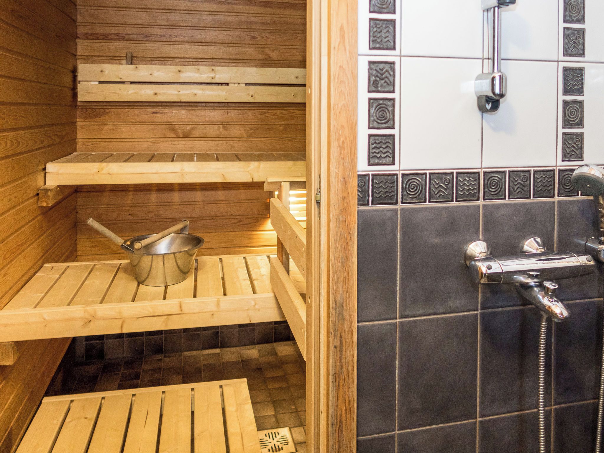 A wooden sauna with a bench, a metal basin, and a shower area with a faucet.