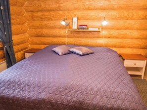 Una habitación de cabaña de madera con una cama, dos lámparas de noche, una mesita auxiliar y una estantería con libros.
