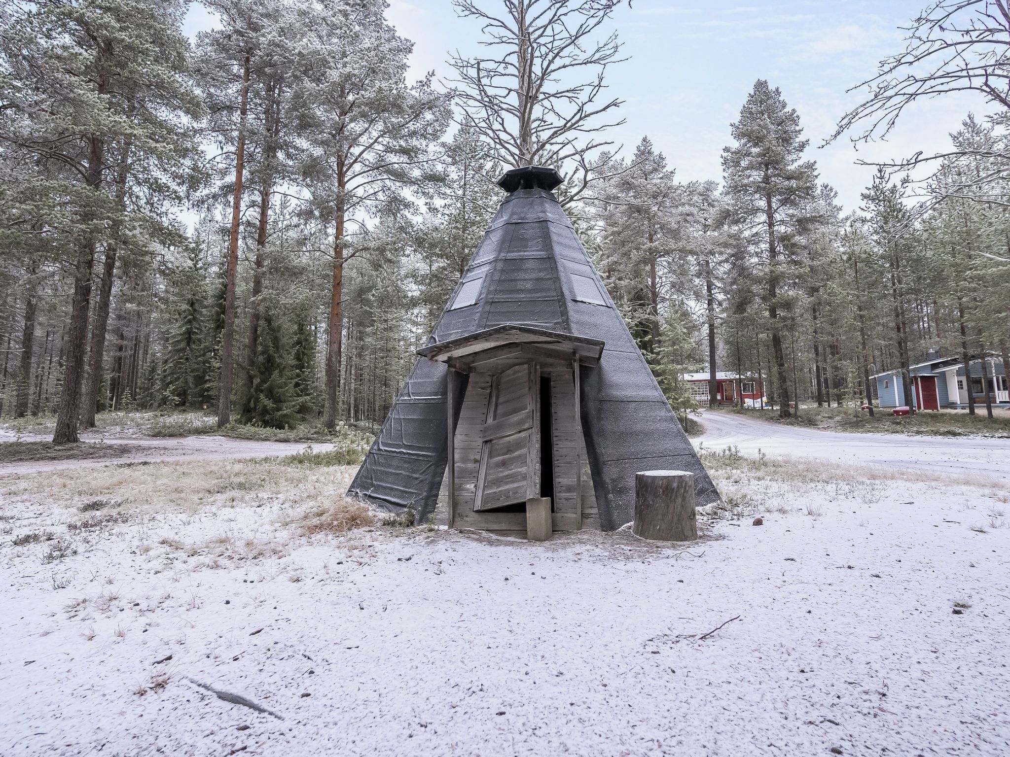 A snow-covered conical structure in a forested area with a dirt ground.