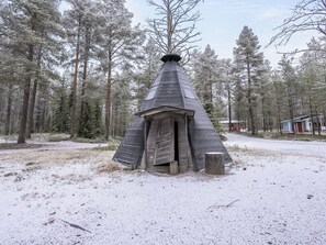 A snow-covered conical structure in a forested area with a dirt ground. - Villa lakka by Interhome (Kuusamo)