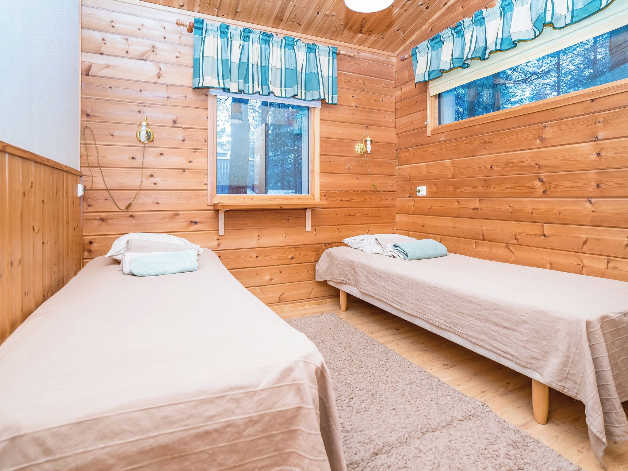 A cabin with two single beds, wooden walls, a window with curtains, and a ceiling light.