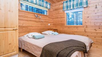 A wooden cabin bedroom with a bed, two windows with curtains, a nightstand, and a wooden wardrobe.