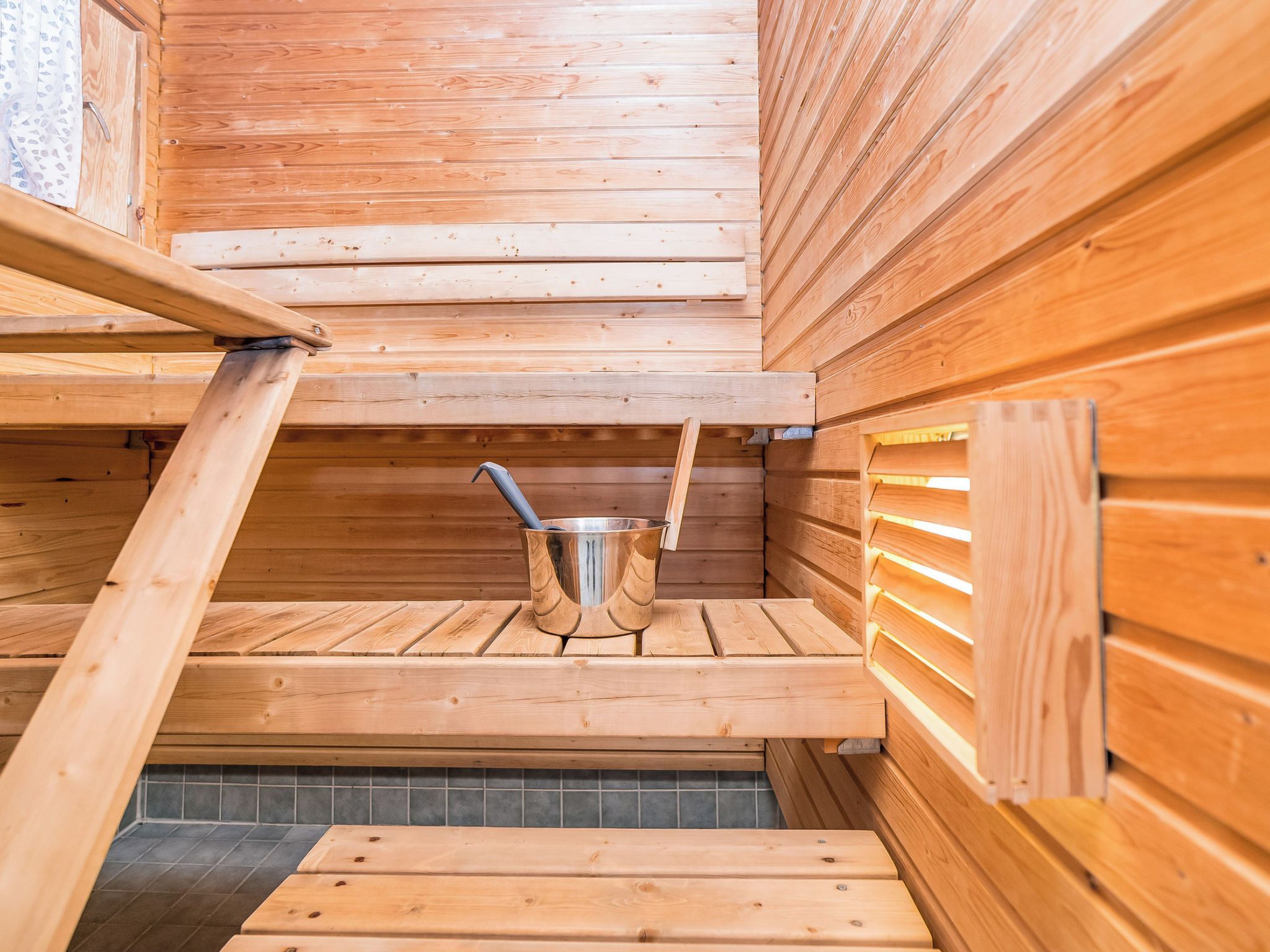 Una sauna con paredes y bancos de madera, un cubo metálico y un piso de baldosas.