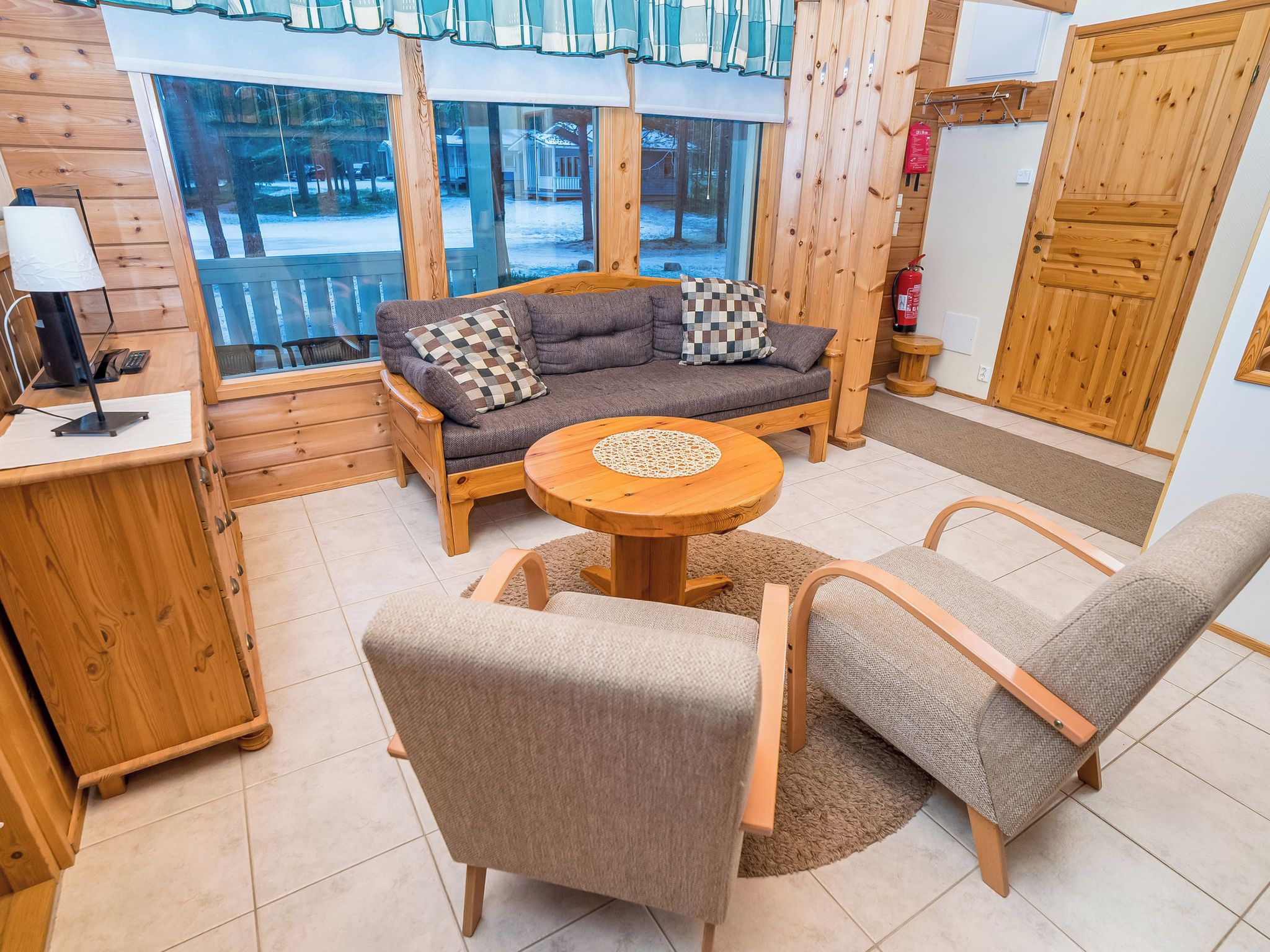 A cozy room with a sofa, two armchairs, a round table, and a window with a view of a snowy landscape.