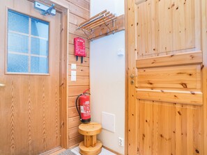 A wooden cabin interior with a window, a fire extinguisher, a small wooden stool, and a clothes drying rack.
