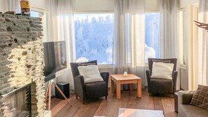 Een gezellige woonkamer met een stenen openhaard, twee fauteuils, een salontafel en een televisie.